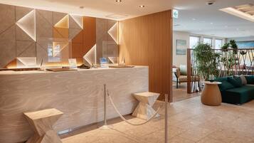 A modern reception area with a geometric wall design, a reception desk, and a seating area with a green sofa and a plant.