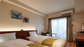Quarto de hotel com duas camas, uma escrivaninha, uma cadeira, uma mesa pequena e uma janela com cortinas.
