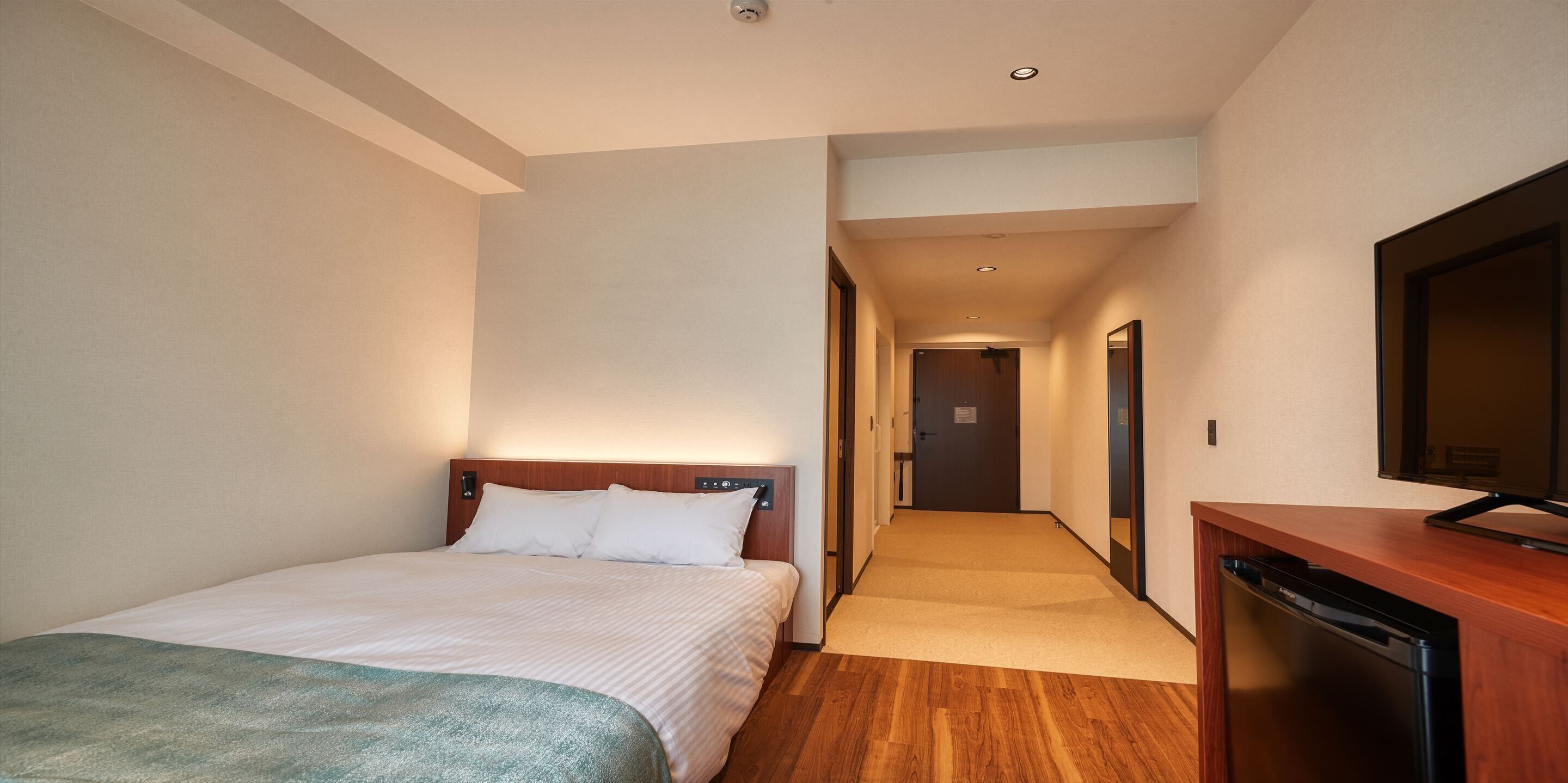 Een hotelkamer met een bed, een televisie, een houten bureau en een gang naar een andere kamer.