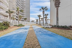 A courtyard with a shuffleboard court, palm trees, and a white fence. - Seaside Beach & Racquet 1210 Salt, Sun & All Fun (Orange Beach)