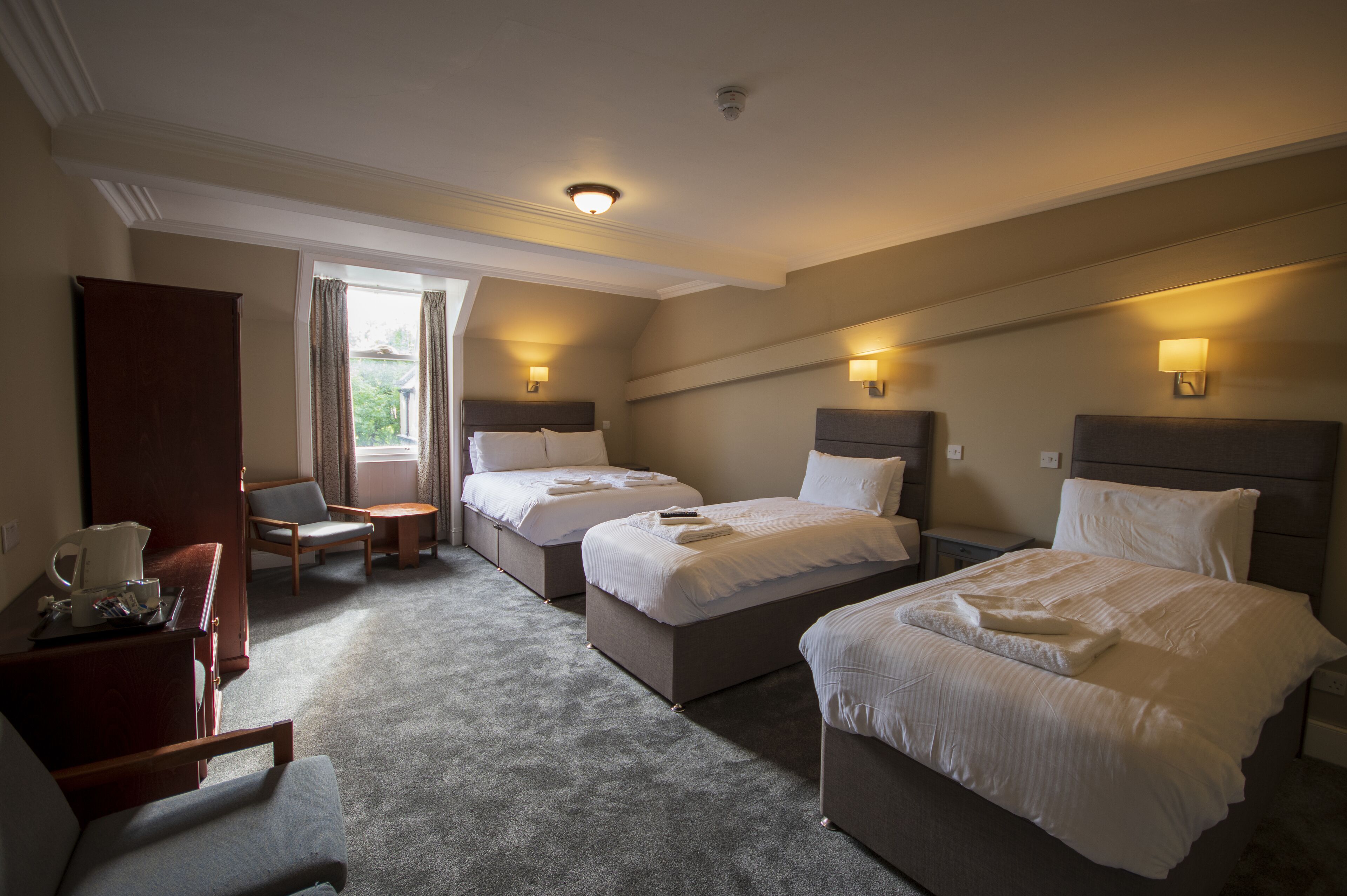 A hotel room with two beds, a desk, a chair, and a window with curtains.