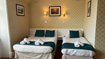 A hotel room with two beds, each with white linens and teal pillows, and two wall-mounted lamps.