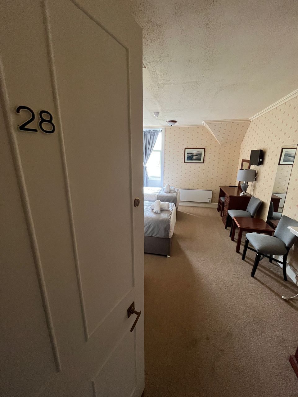 Une chambre d’hôtel avec un lit, un bureau, deux chaises, une lampe et une petite table.