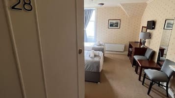 Une chambre d’hôtel avec un lit, un bureau, deux chaises, une lampe et une petite table.