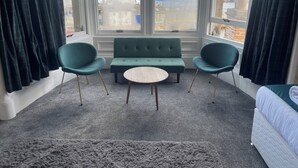 Una habitación con un ventanal grande, un sofá verde, dos sillas verdes y una mesa redonda.