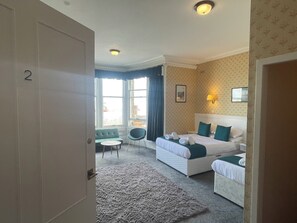 A hotel room with a large bed, a smaller bed, a sofa, a chair, and a view of the city through large windows. - The Stromness Hotel (Stromness)