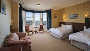 Habitación de hotel con dos camas, un sofá, una silla, una mesita y vistas al mar.