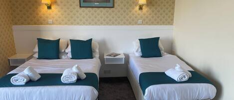 Habitación de hotel con dos camas, cada una con una almohada, una mesita de noche y una lámpara. Hay un cuadro enmarcado en la pared sobre las camas.