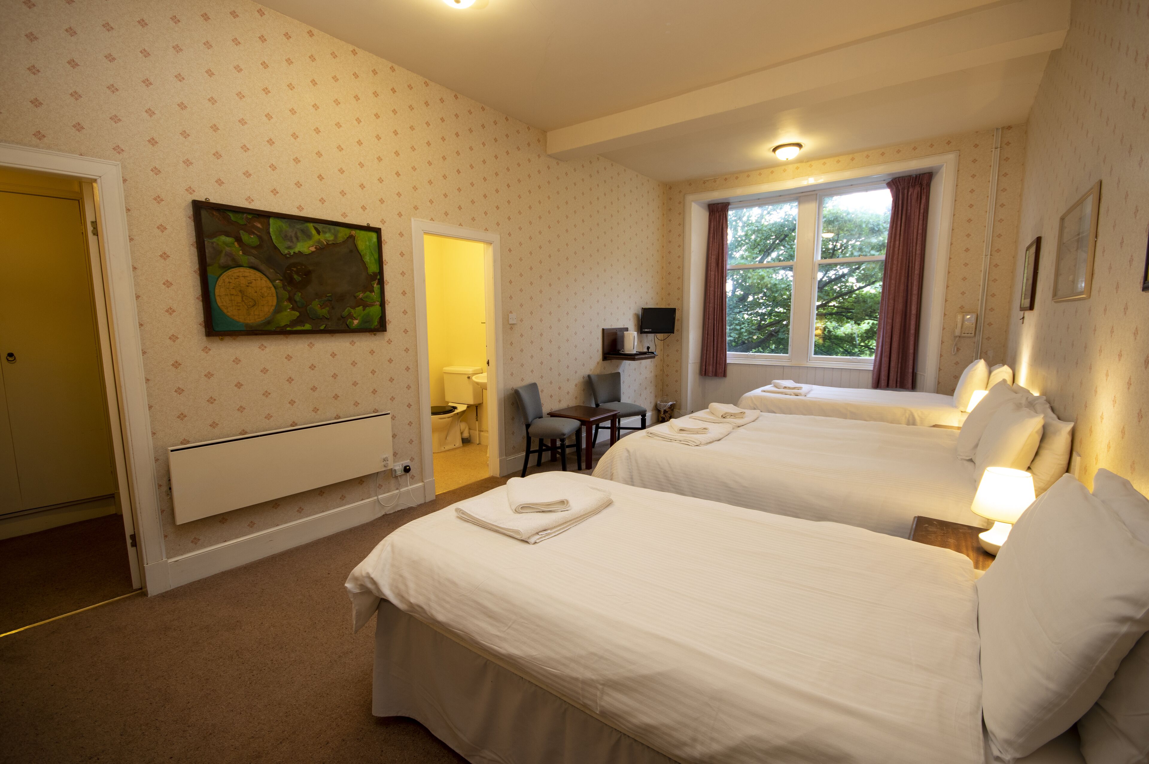 A hotel room with two beds, a desk, a chair, a TV, and a window with curtains.