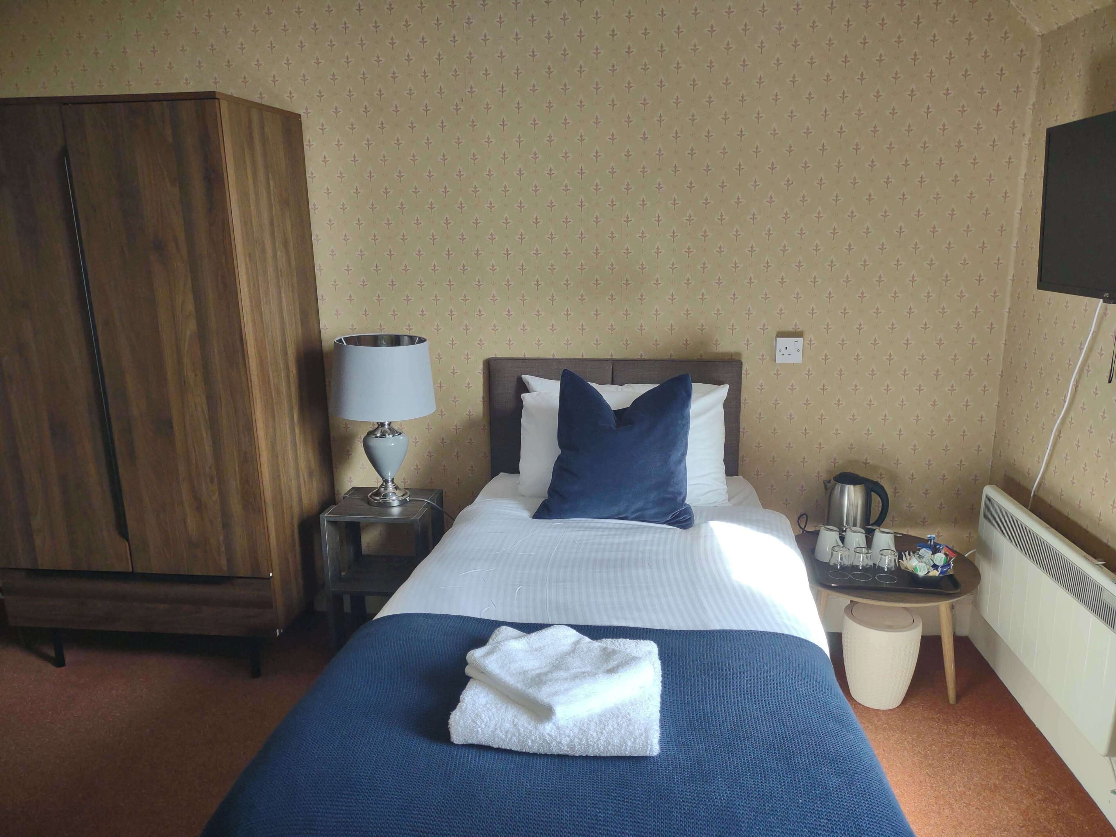 A hotel room with a bed, a nightstand, a lamp, a wardrobe, and a radiator.