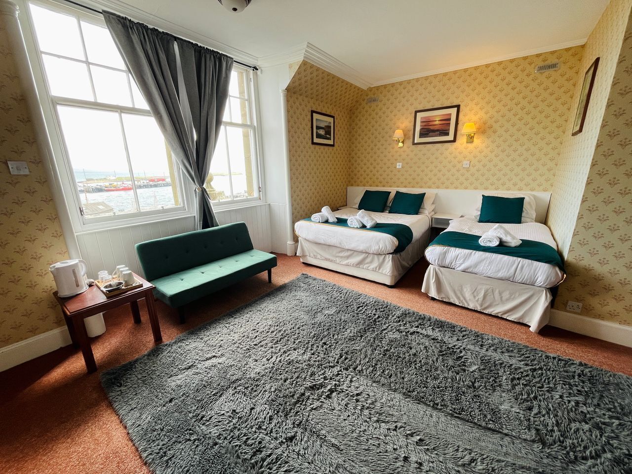 Una habitación de hotel con dos camas, un sofá verde, un tapete grande y una ventana con cortinas.