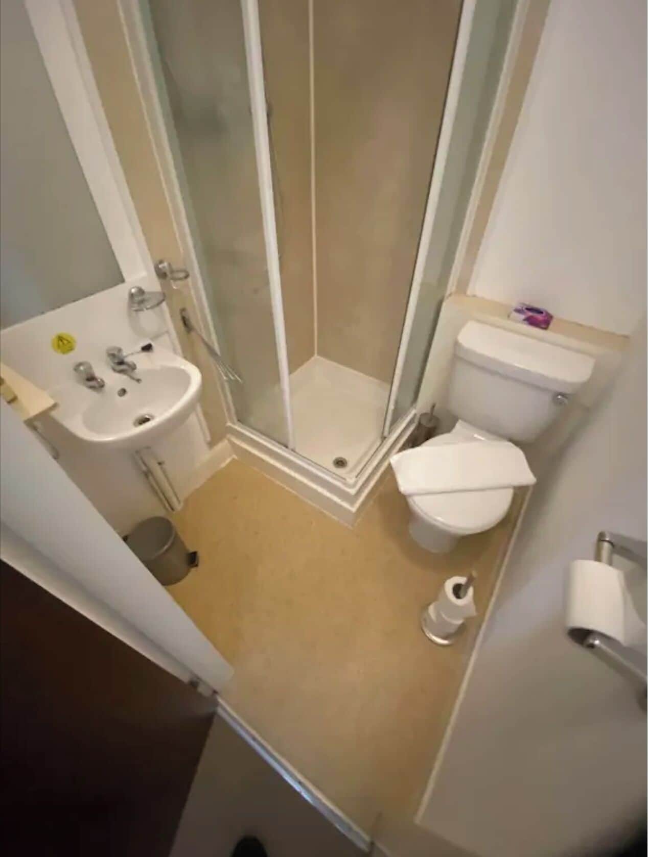 Un baño pequeño con ducha, inodoro, lavabo y un cubo de basura pequeño.