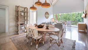 A dining area with a round table, wicker chairs, and hanging rattan light fixtures.