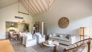 A spacious living area with a sofa, coffee table, and wicker chair. A kitchen is visible in the background.