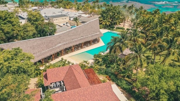 A resort with a pool, thatched-roof buildings, and palm trees.