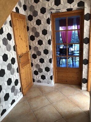 A room with a geometric patterned wall, a wooden door, and a view through a window with purple curtains.