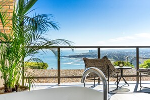 A balcony with a view of the ocean, a white bathtub, and wicker furniture. - Zaria Sun Family (Cape Town)