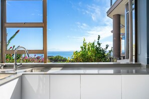 A modern kitchen with a large window overlooking a scenic view of the sea and lush greenery.