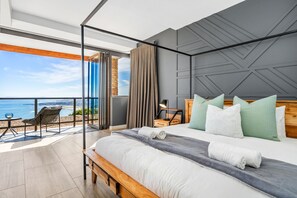 Een moderne slaapkamer met een groot bed, een balkon met uitzicht op zee en een houten hoofdeinde.