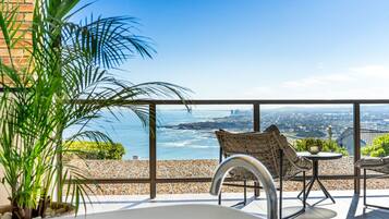 A balcony with a view of the ocean, a white bathtub, and wicker furniture.