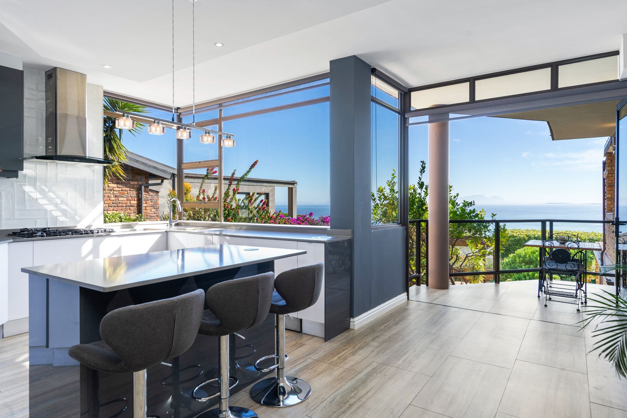 A modern kitchen with a large island, bar stools, and a view of the ocean.