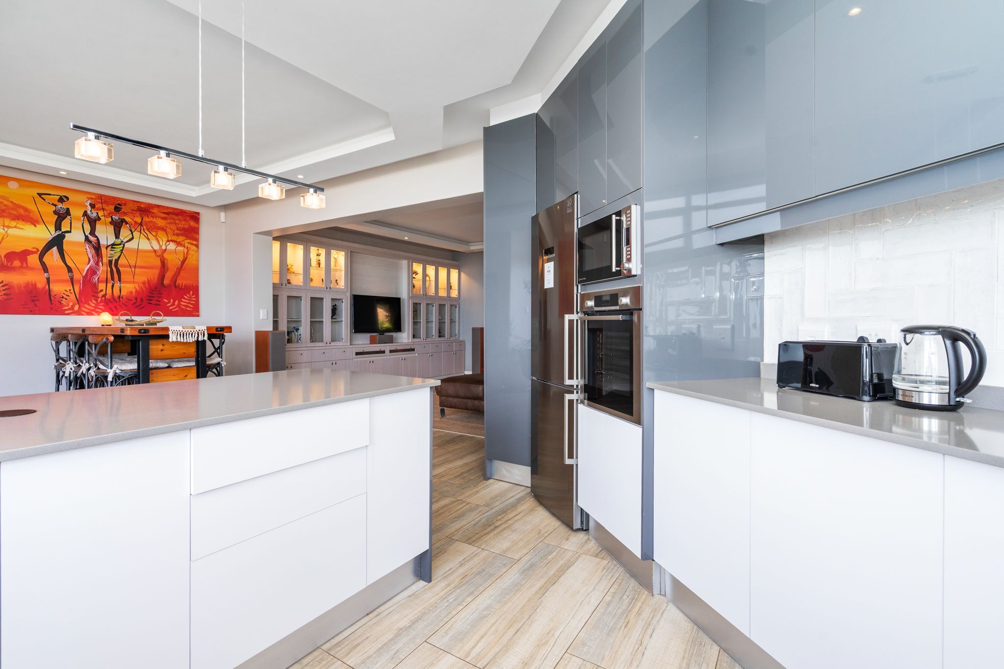 Une cuisine moderne dotée d’un îlot central, d’appareils électroménagers en acier inoxydable et d’un grand tableau accroché au mur.