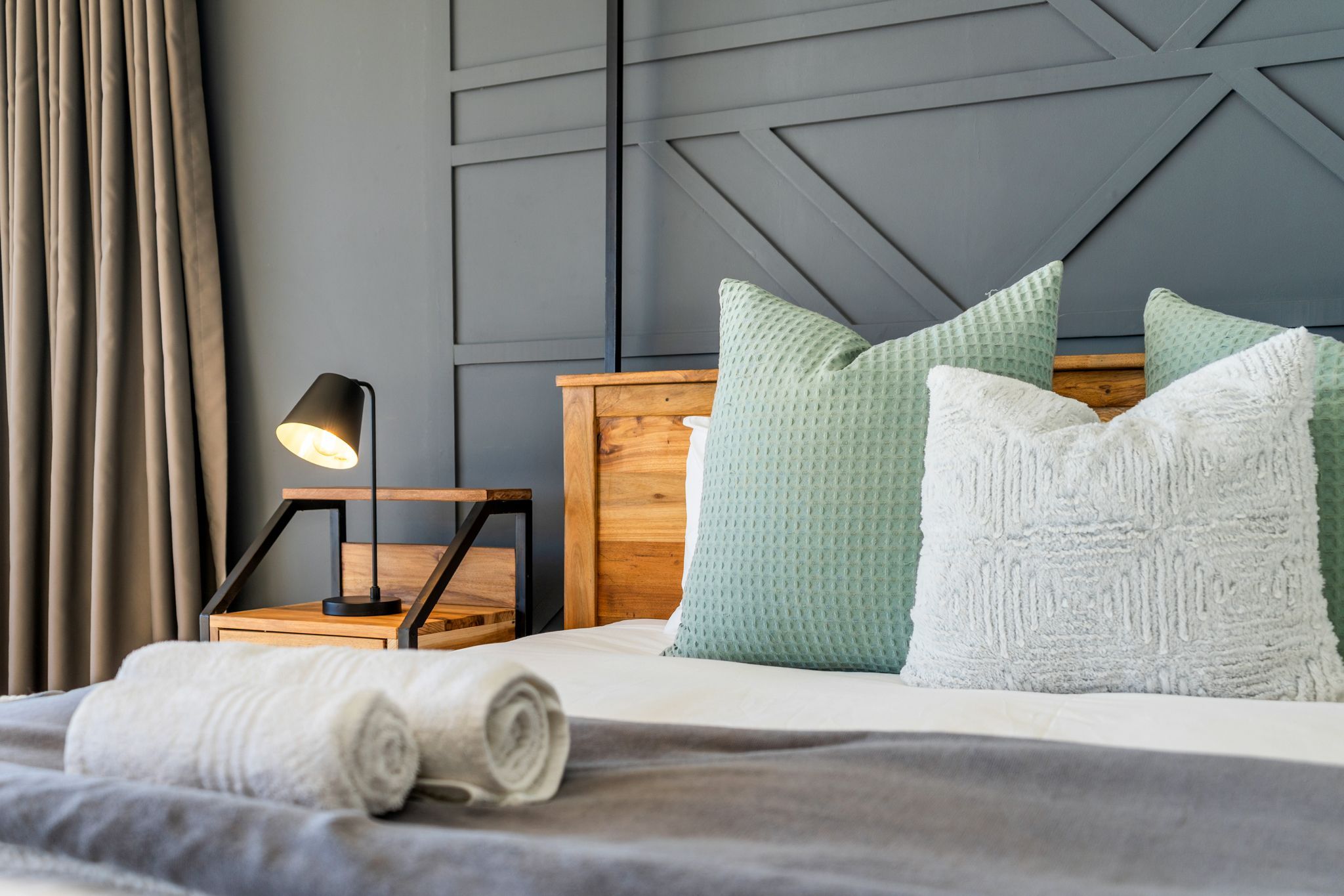 A neatly made bed with a wooden headboard, a bedside lamp, and two pillows.