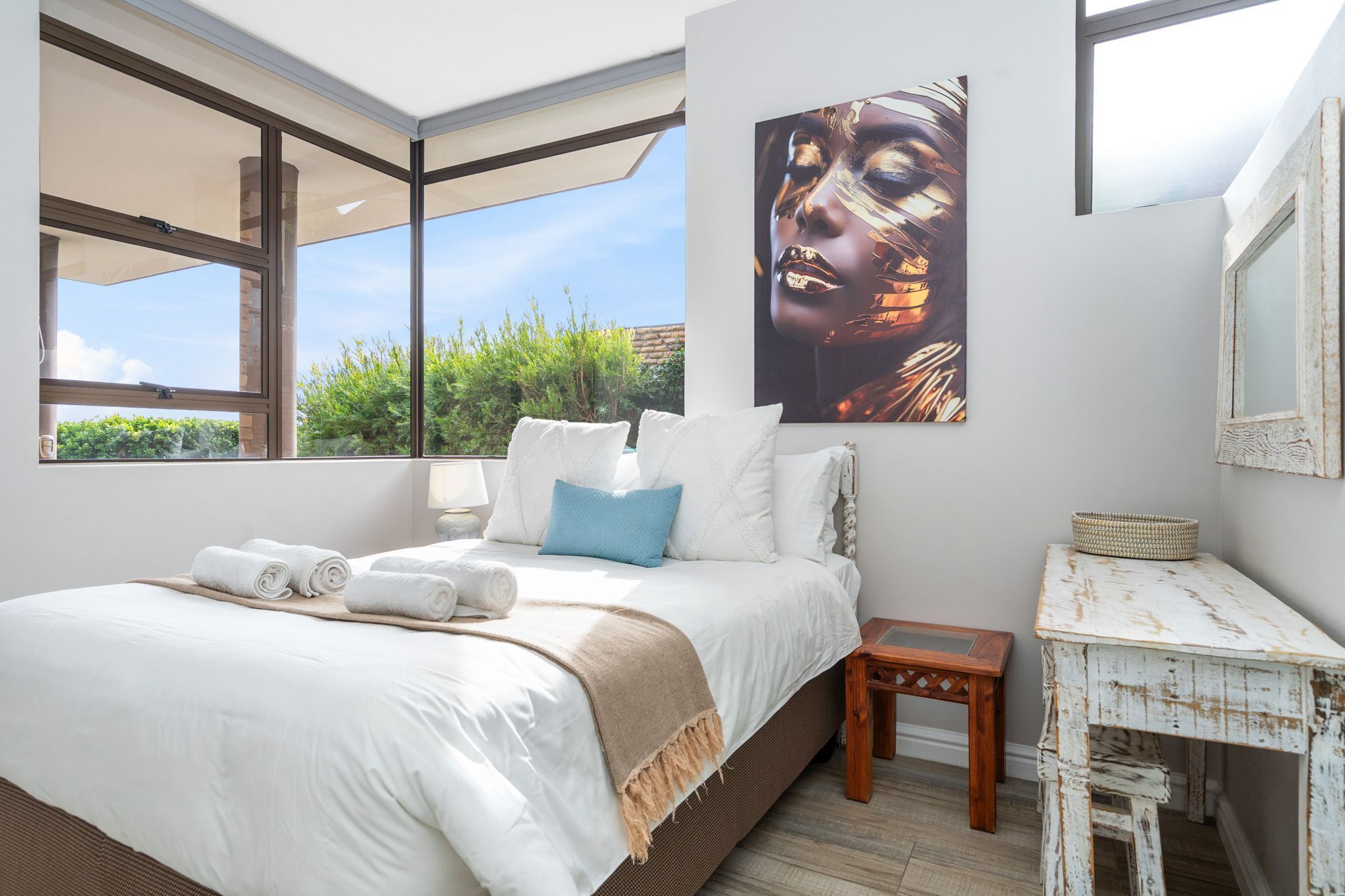 A bedroom with a large bed, a small table, and a painting on the wall.