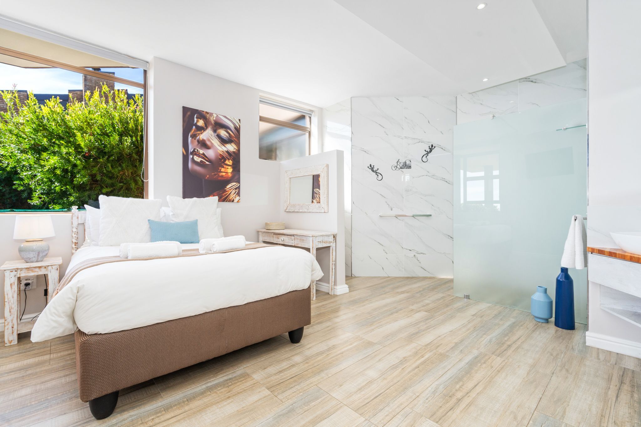 A modern bedroom with a large bed, a small bedside table, a mirror, and a glass shower enclosure.