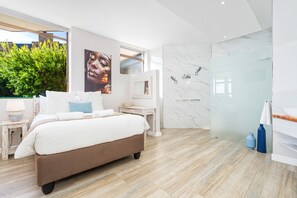 A modern bedroom with a large bed, a small bedside table, a mirror, and a glass shower enclosure.