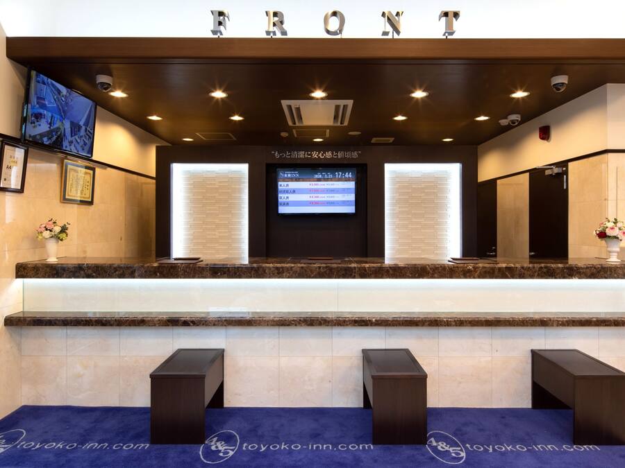 Zona de recepción de hotel con pantalla digital, mostrador de mármol y escritorio.