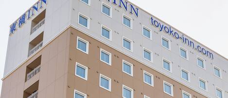 Un immeuble hôtelier à plusieurs étages, dont la façade porte les enseignes « TOYOKO INN » et « toyoko-inn.com ».