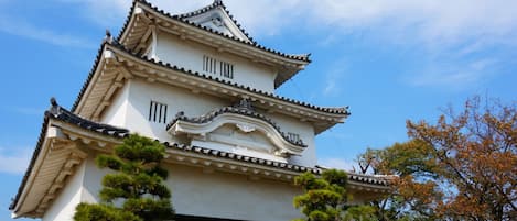 A traditional Japanese castle with multiple tiers, surrounded by well-maintained gardens and trees.