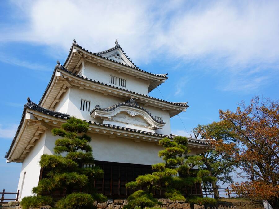 A traditional Japanese castle with multiple tiers, surrounded by well-maintained gardens and trees.