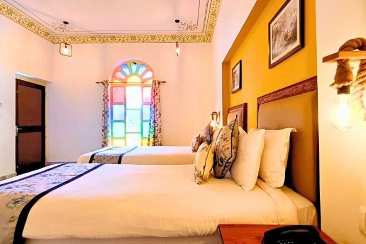 Een hotelkamer met twee bedden, een groot raam met gordijnen en een wandlamp.