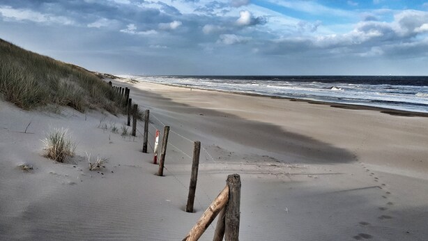 A sandy beach with a wooden fence and dunes in the background. - 'Het Melkhuis', the tiny house that makes you happy😀 (Katwijk aan Zee)