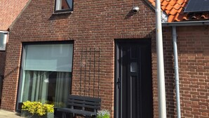 A brick building with a black door, a bench, and a street lamp. - 'Het Melkhuis', the tiny house that makes you happy😀 (Katwijk aan Zee)