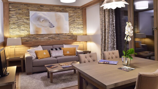 A modern living room with a stone wall, a large polar bear painting, a dining table, and a sofa with decorative pillows. - Charming apartment with parking and pets allowed, near slopes (Courchevel 1550)