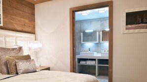A bedroom with a bed, bedside table, lamp, and a view into the bathroom with a sink and mirror. - Charming apartment with parking and pets allowed, near slopes (Courchevel 1550)