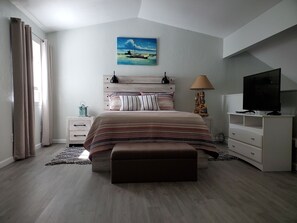 Een slaapkamer met een bed, een televisie, een lamp en een schilderij aan de muur.