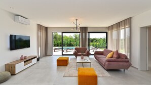 Ein geräumiges Wohnzimmer mit großem Flachbildfernseher, bequemen Sitzgelegenheiten und Blick auf einen Pool.