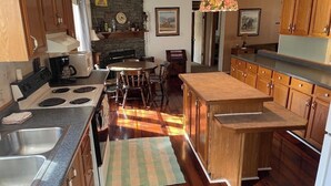 A kitchen with wooden cabinets, a stone wall, a dining area with a table and chairs, and a hanging light fixture. - Cabana Too Smith Mountain Lake (Moneta)