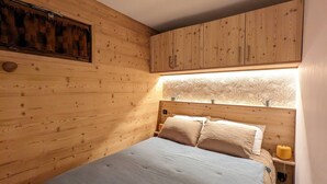 Une pièce en bois avec un lit, des murs en bois et une fenêtre donnant sur des arbres.