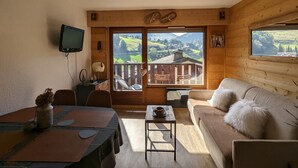Une pièce chaleureuse au décor intérieur en bois, comprenant un coin repas, un canapé et de grandes fenêtres donnant sur un paysage montagneux.
