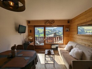 Um quarto acolhedor com decoração em madeira, área de jantar, sofá e janelas amplas com vista para uma paisagem montanhosa.