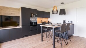 A modern kitchen with dark cabinetry, a built-in oven, and a dining area with a table and chairs. - Gîtes with heated pool near beach. Garden, spa, BBQ, WiFi. Baby bed included (Préfailles)
