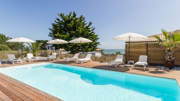 A swimming pool with wooden deck, white lounge chairs, and umbrellas. - Gîtes with heated pool near beach. Garden, spa, BBQ, WiFi. Baby bed included (Préfailles)