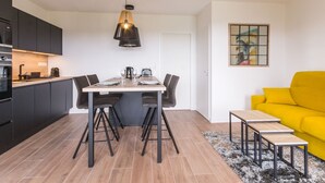 A modern kitchen with dark cabinets, a dining table with chairs, a yellow sofa, and a painting on the wall. - Gîtes with heated pool near beach. Garden, spa, BBQ, WiFi. Baby bed included (Préfailles)