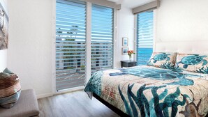 A bedroom with a large bed, a ceiling fan, and a view through the window blinds. - Alii Villas #332 Million Dollar Ocean View. Watch Dolphins, Coastal Vibes. (Kailua-Kona)