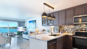 A modern kitchen with a large island, stainless steel appliances, and a view of the sea. - Alii Villas #332 Million Dollar Ocean View. Watch Dolphins, Coastal Vibes. (Kailua-Kona)